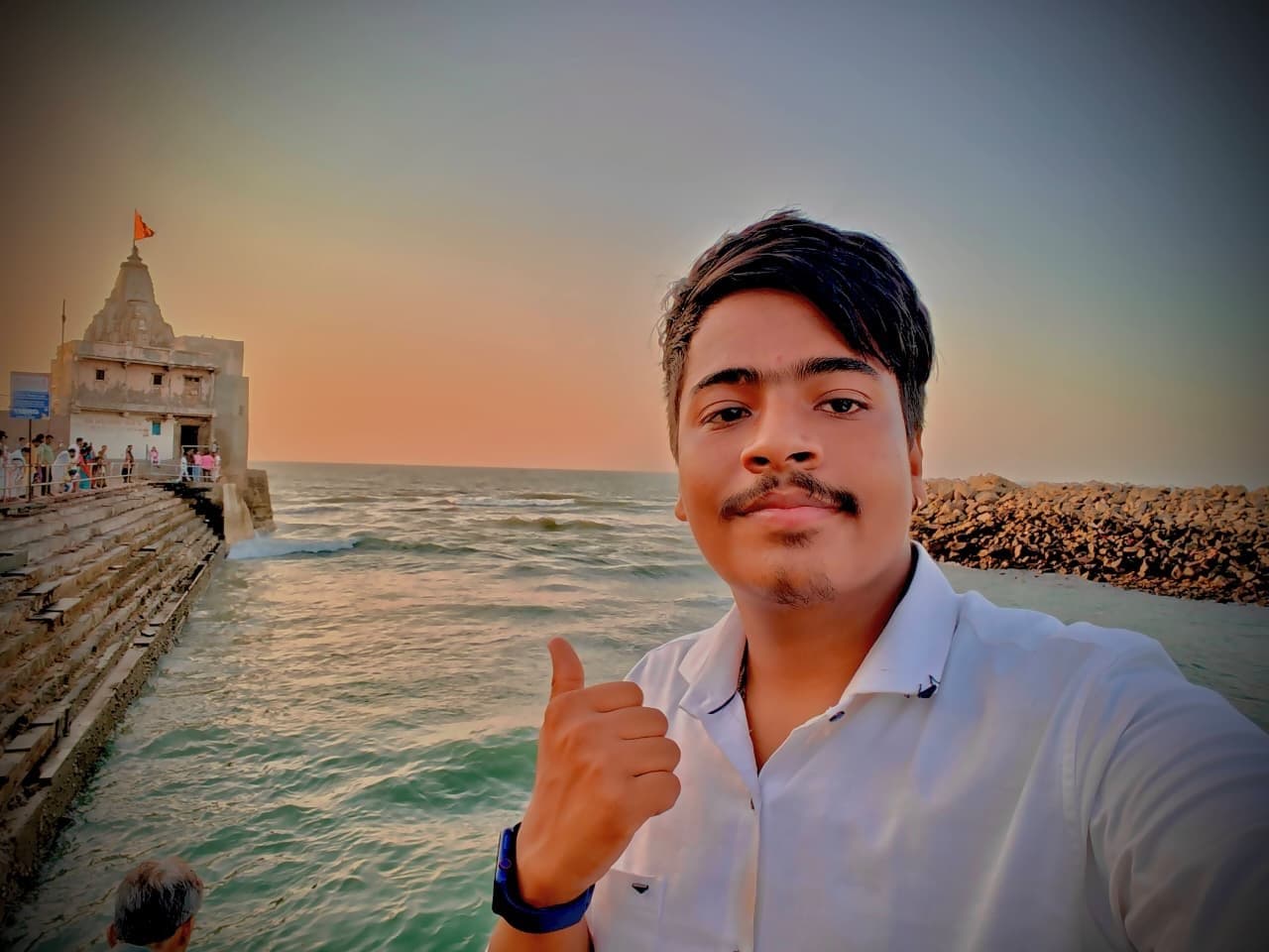 Shubh taking a selfie by the sea at sunset, a temple on the shore behind him